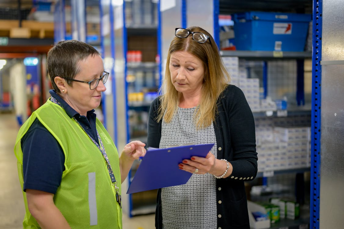 employees looking at the clipboard while standing near metal shelves