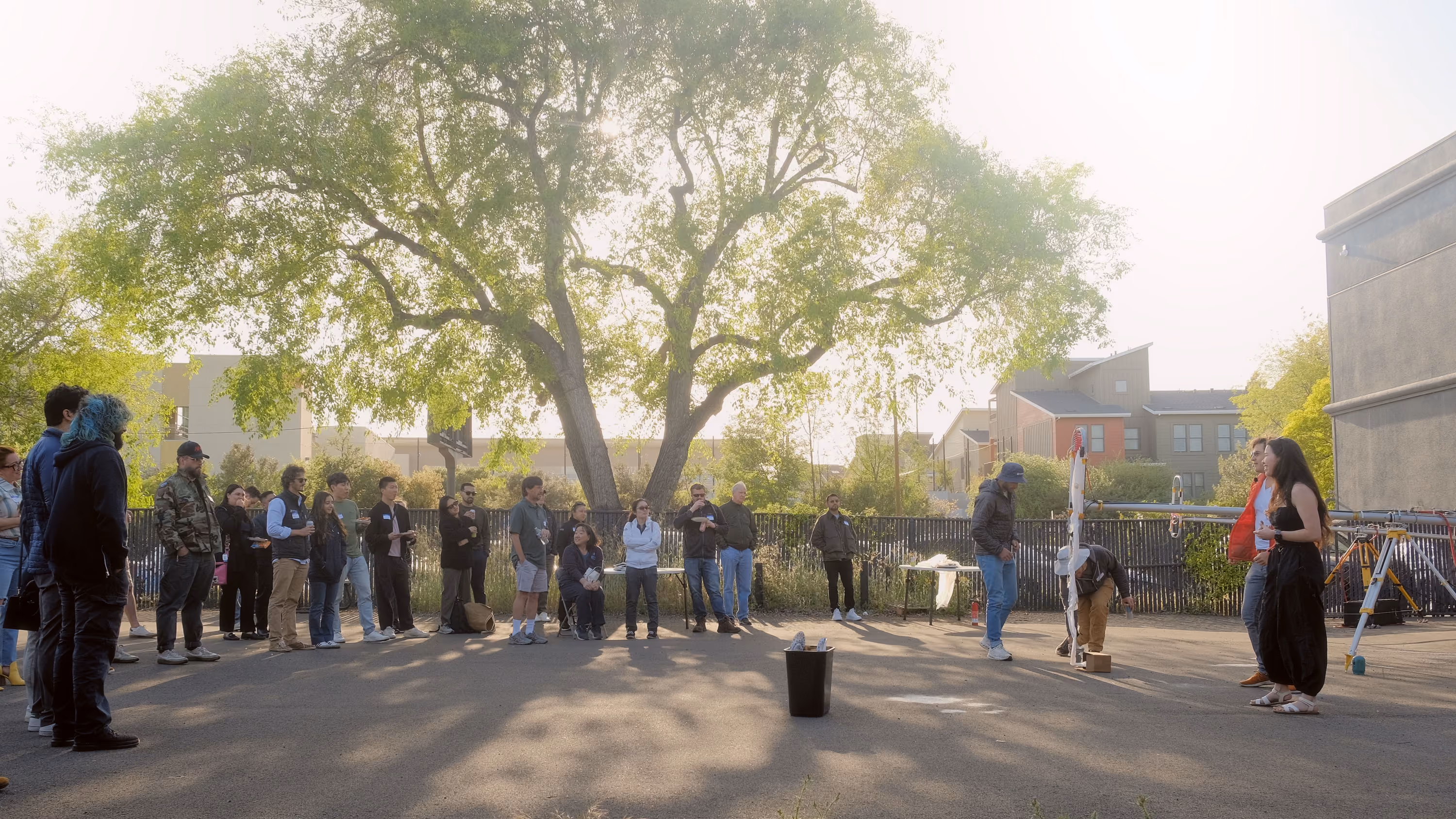 Group of people standing in a well-lit parking lot that are watching a balloon launch