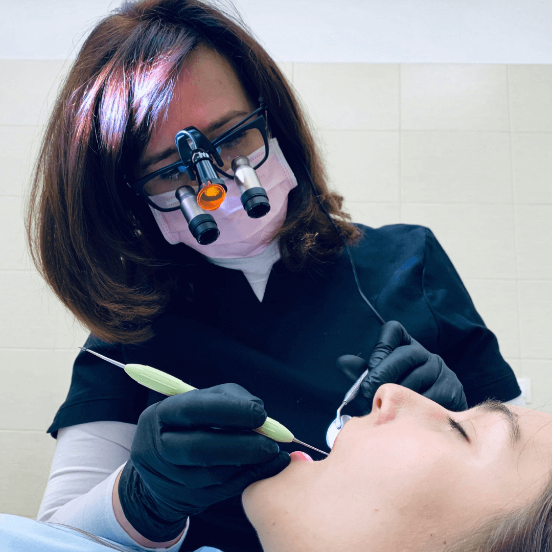 a woman in a mask and gloves using a dental tool to insert a tooth