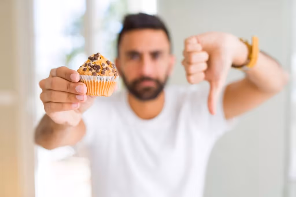 Un hombre mostrando un cupcake en la mano haciendo señal de no recomendable