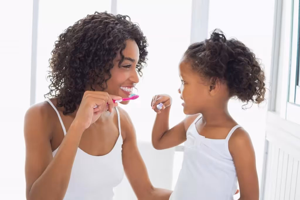 Mamá e hija cepillándose los dientes con un cepillo de dientes.