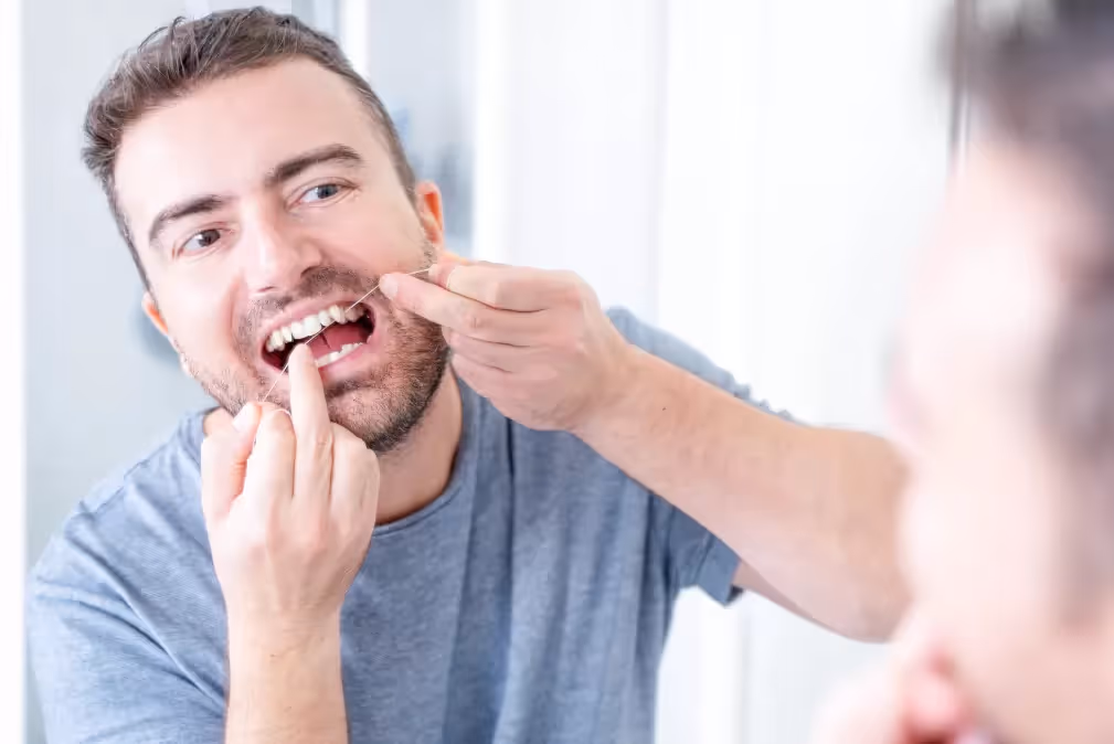 Hombre utilizando el hilo dental para limpiar sus dientes