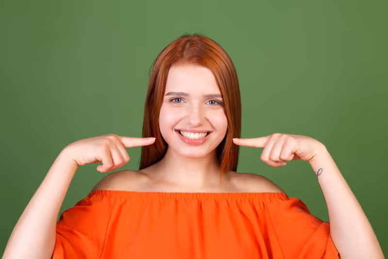 Chica sonriendo señalando sus dientes