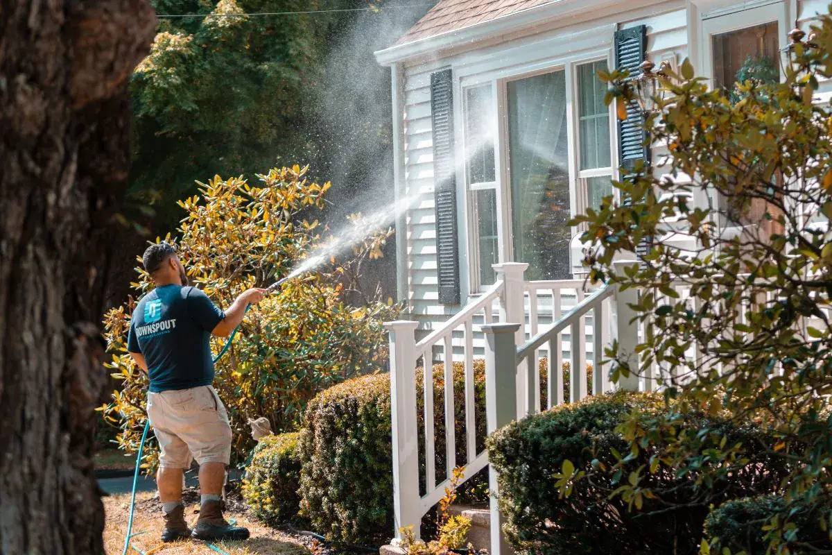 A Downspout crew member pressure washing the front of a white house
