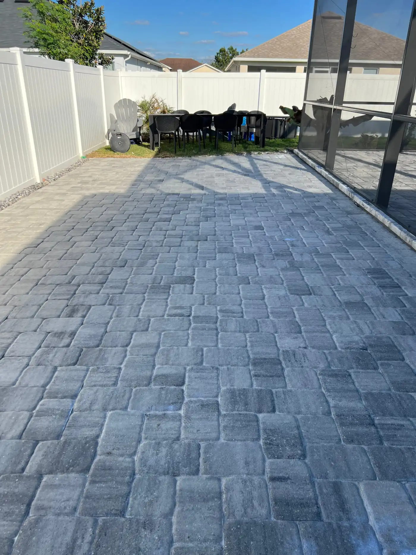 A sealed gray paver patio beside a screened lanai and a white fence, finished by Southern Pro Wash and Seal