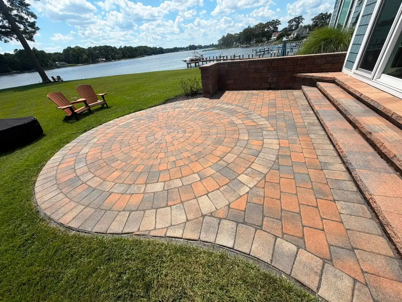 A circular paver patio with steps beside a lawn and a lake, finished by Thumbs Up Paver Sealing