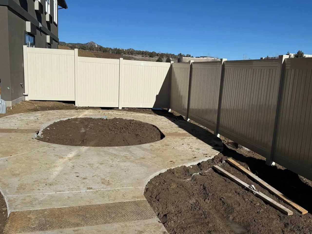 A two tone vinyl privacy fence beside a new concrete patio, installed by Four Corners Fence and Patio