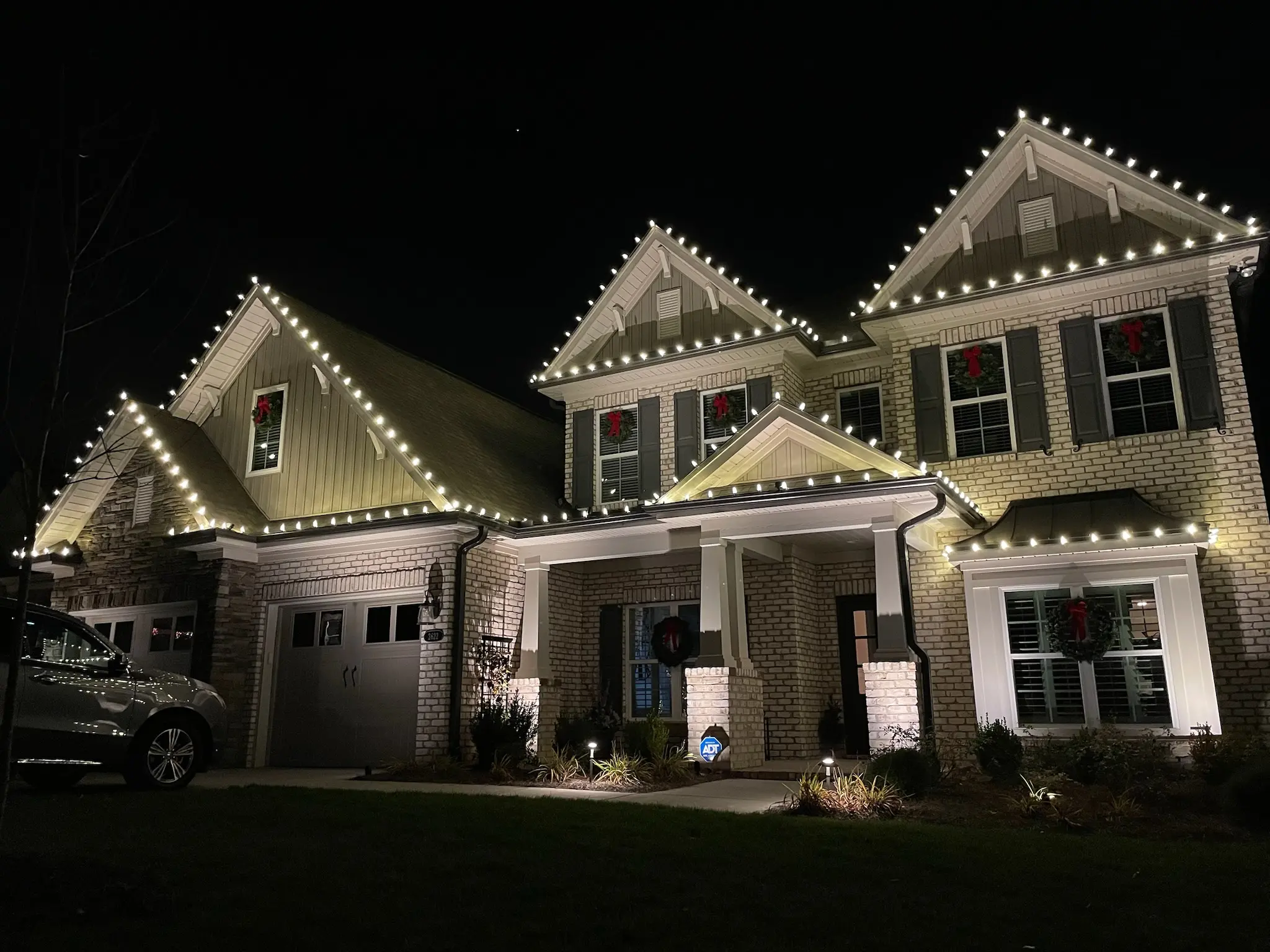 Two-story home outlined in white Christmas lights at night