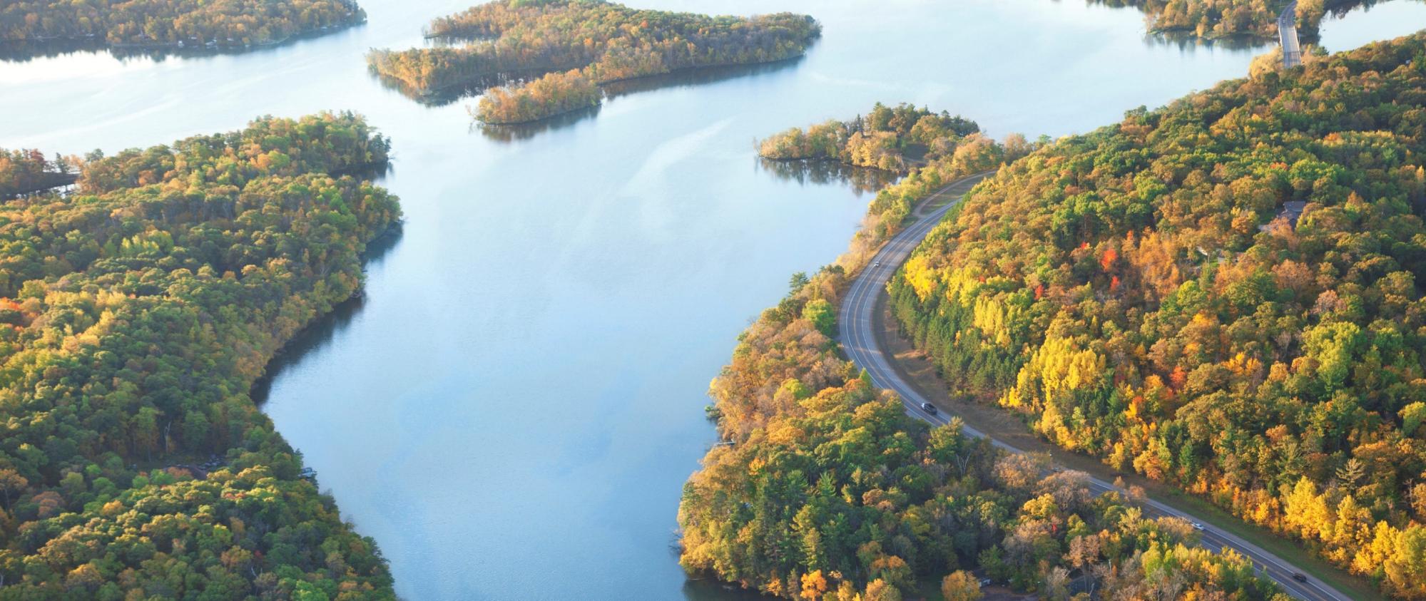 A winding road goes along the shore of a calm lake with several small islands.