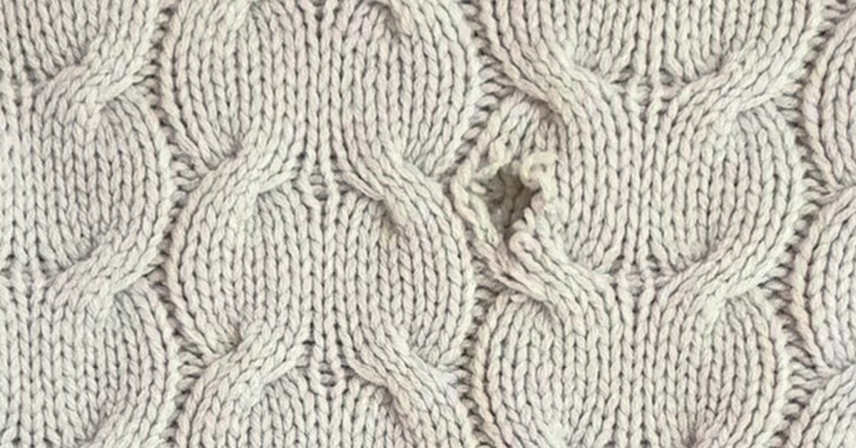 Moth hole in a cream cable knit sweater