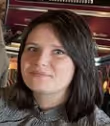 Vrouw met donkerbruin haar, zittend en licht glimlachend.