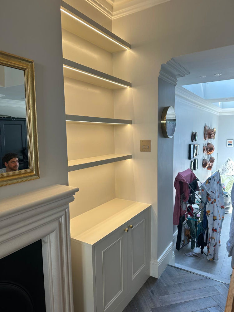 Alcove Units with shaker cabinets below and floating shelving above. Painted White with LED under light. Either side of traditional fireplace with gold framed mirror above.