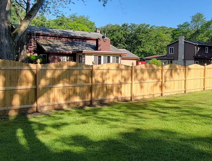 A picture of a white vinyl privacy fence with vertical planks and decorative post caps.