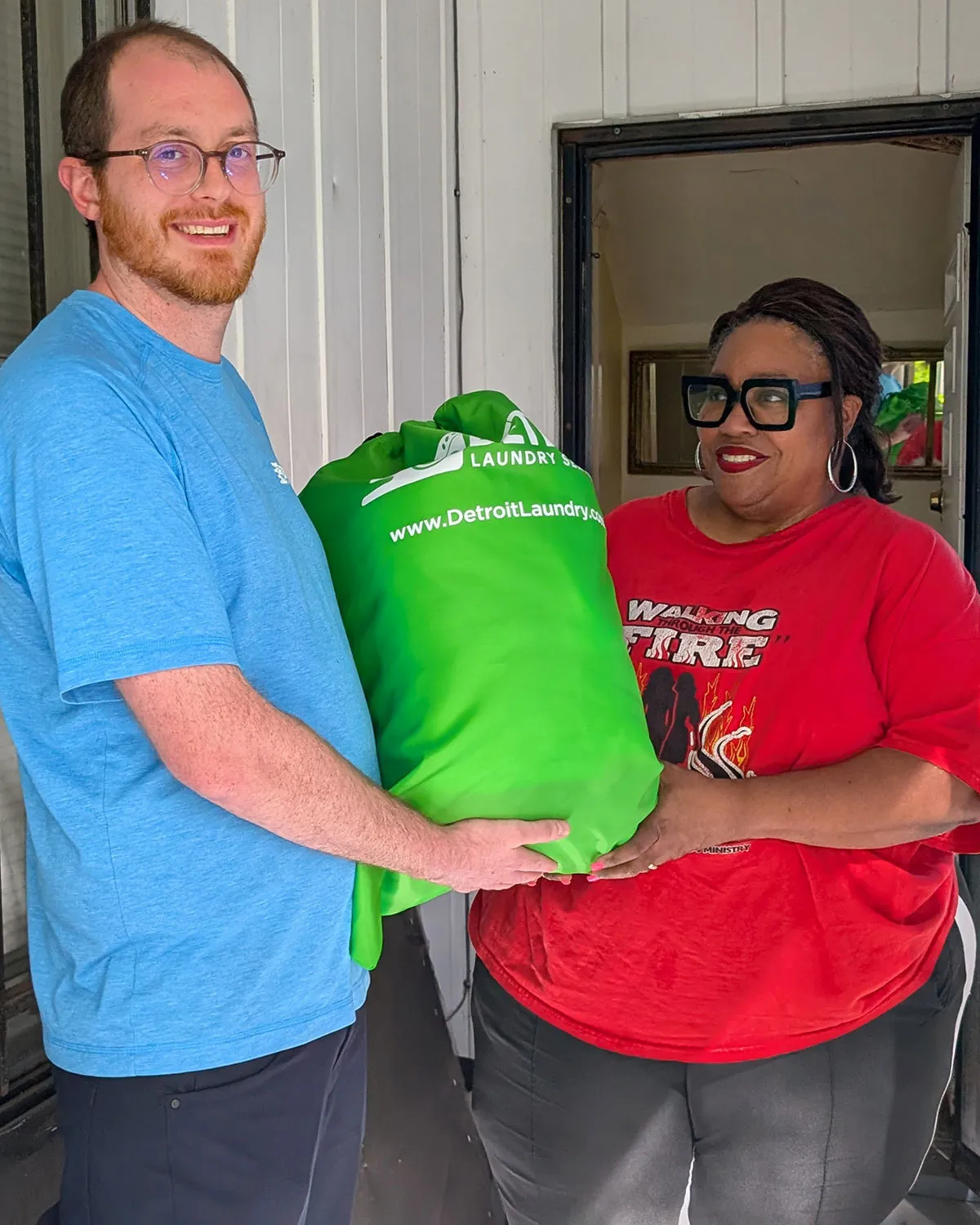 Detroit Laundry Service team member handing a green laundry bag to a smiling customer