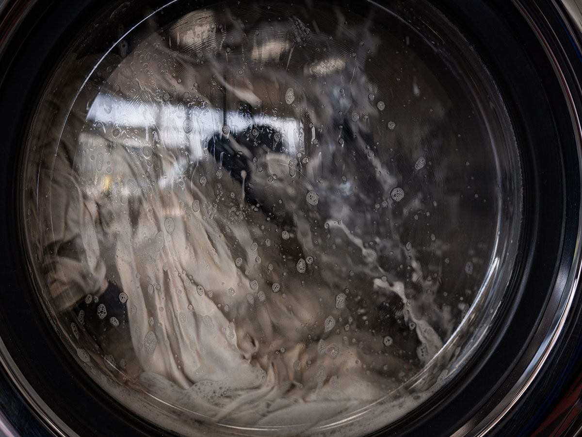 View through a washer door of clothes tumbling in soapy water