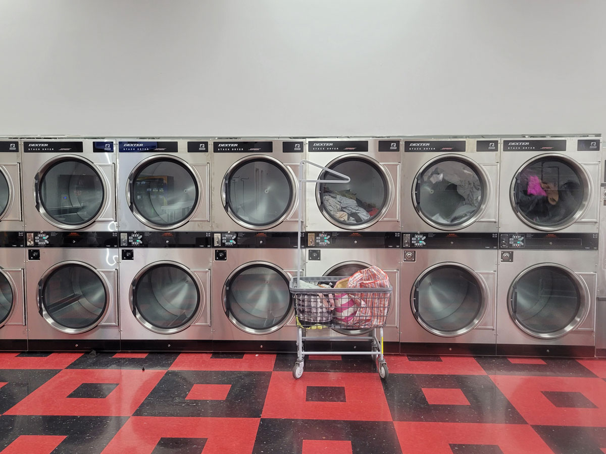 Wall of stacked commercial dryers in a laundromat with a laundry cart in front