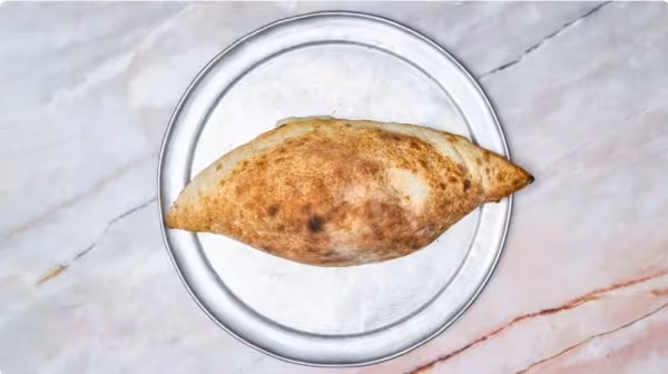 Top view of a baked calzone on a clear glass plate placed on a white marble surface.