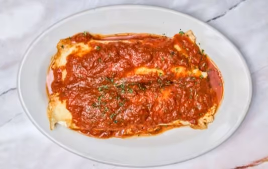 Plate of lasagna with rich tomato sauce and sprinkled herbs on top, served on a white oval dish.
