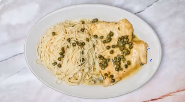White plate with two pieces of chicken breast topped with green peppercorn sauce and a serving of thin spaghetti pasta topped with green peppercorns, placed on a marble surface.