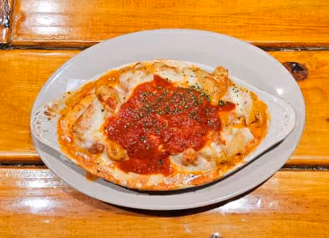 Baked dish with melted cheese topped with red tomato sauce and sprinkled herbs, served in an oval white ceramic dish on a wooden table.