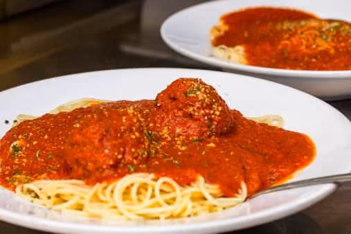 Two white plates of spaghetti topped with red tomato sauce and meatballs, with one plate in the foreground and another blurred in the background.