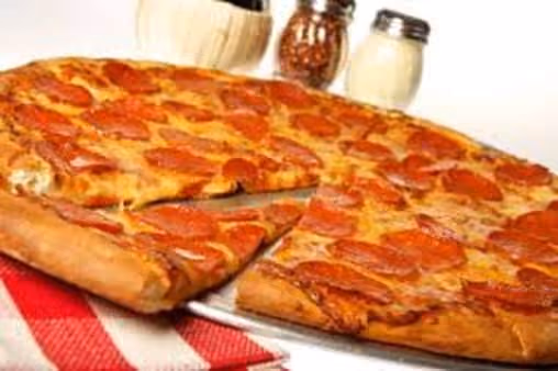 Pepperoni pizza with one slice slightly pulled out on a white plate, set on a red and white checkered cloth with condiment shakers in the background.