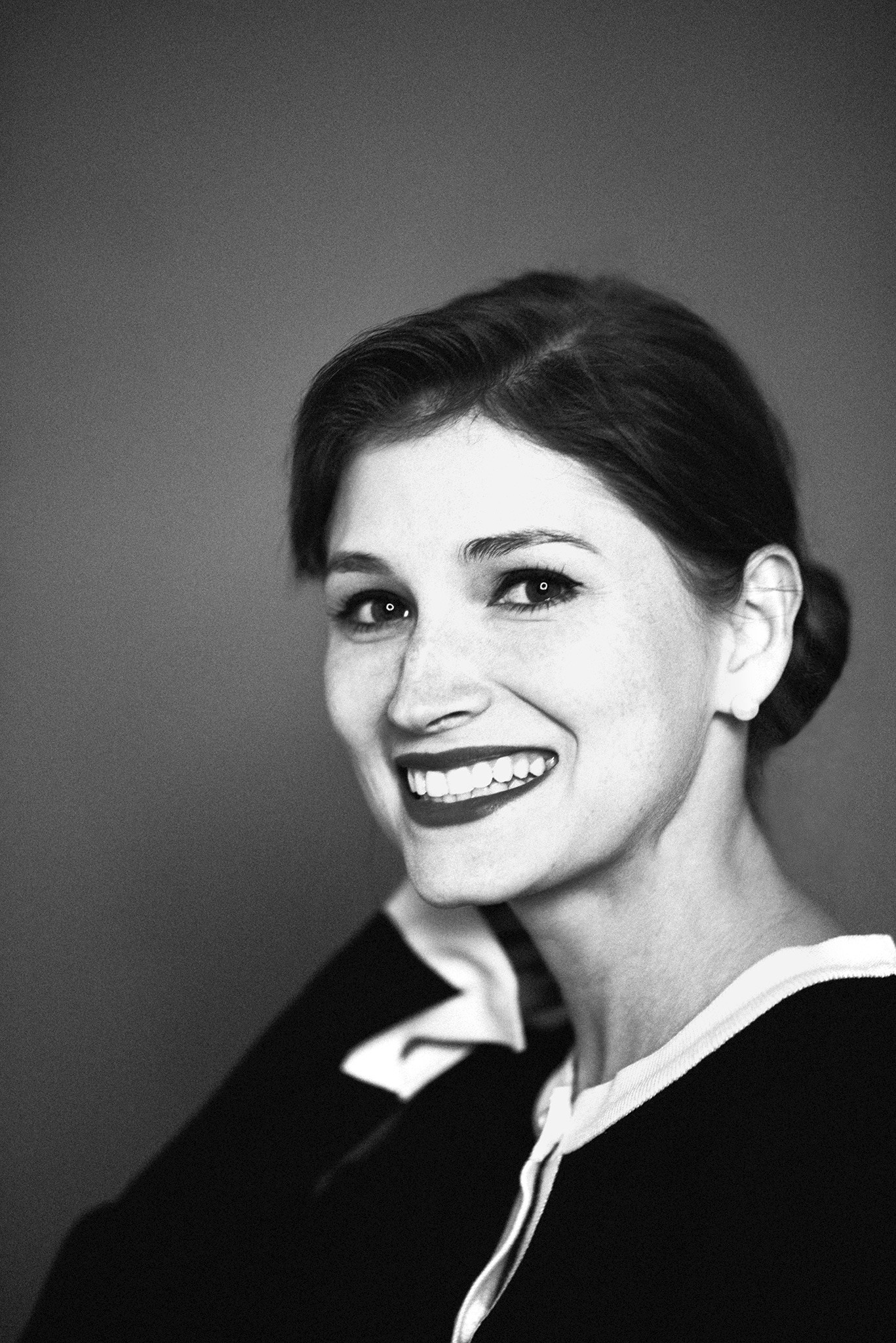 Black and white portrait of a smiling woman with neatly tied hair, exuding warmth and elegance