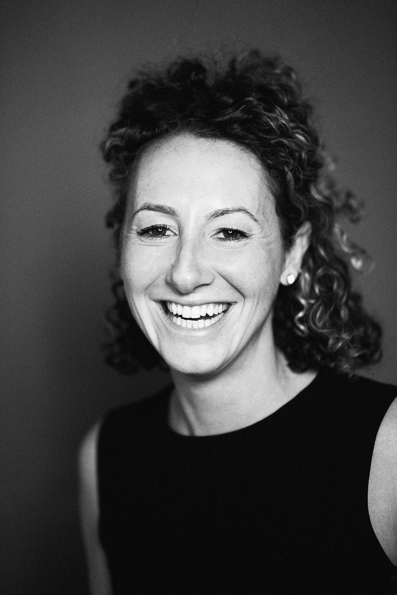 A woman with curly hair and a black shirt smiling.
