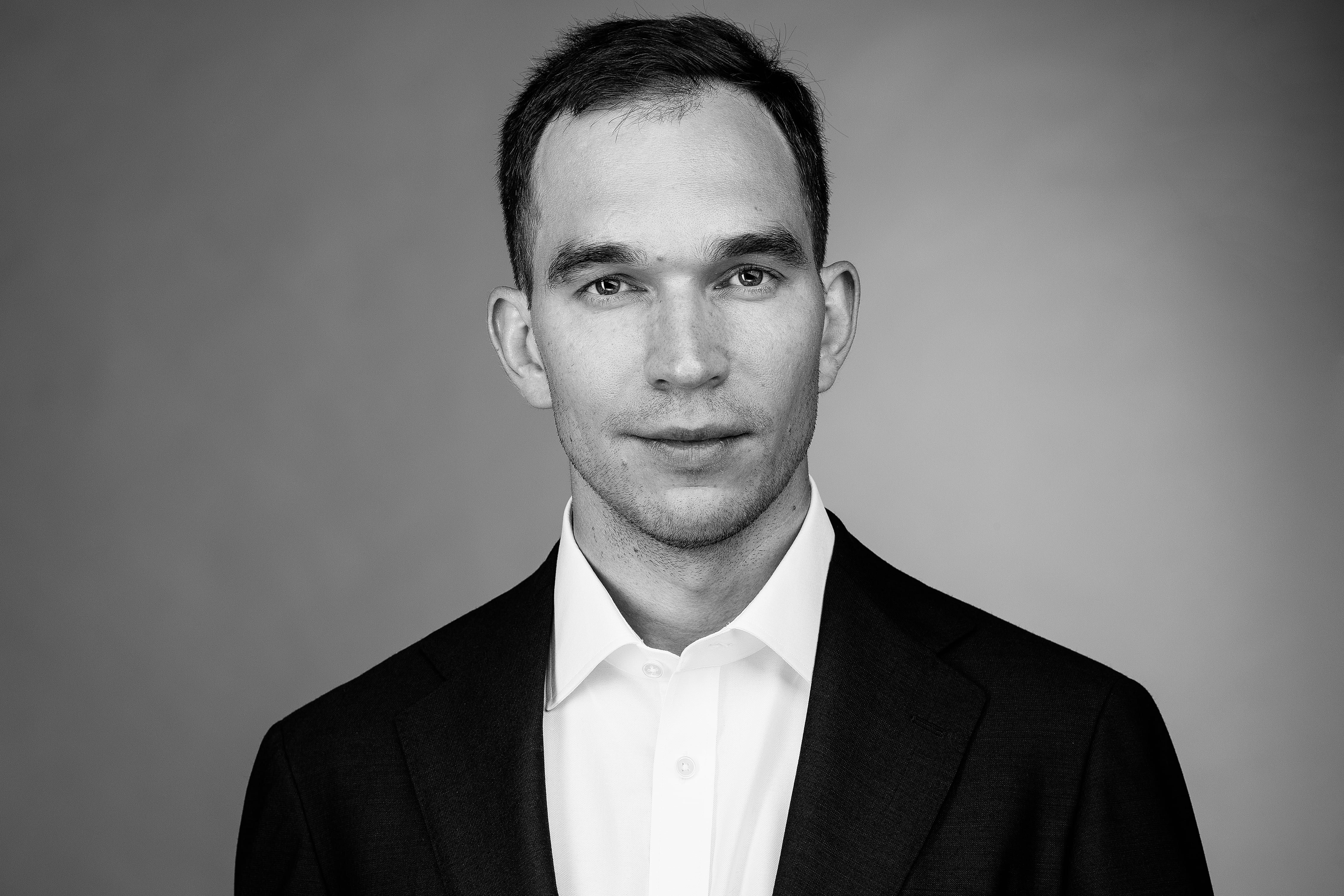 Black and white portrait of a man in a suit and white shirt, facing the camera with a neutral expression