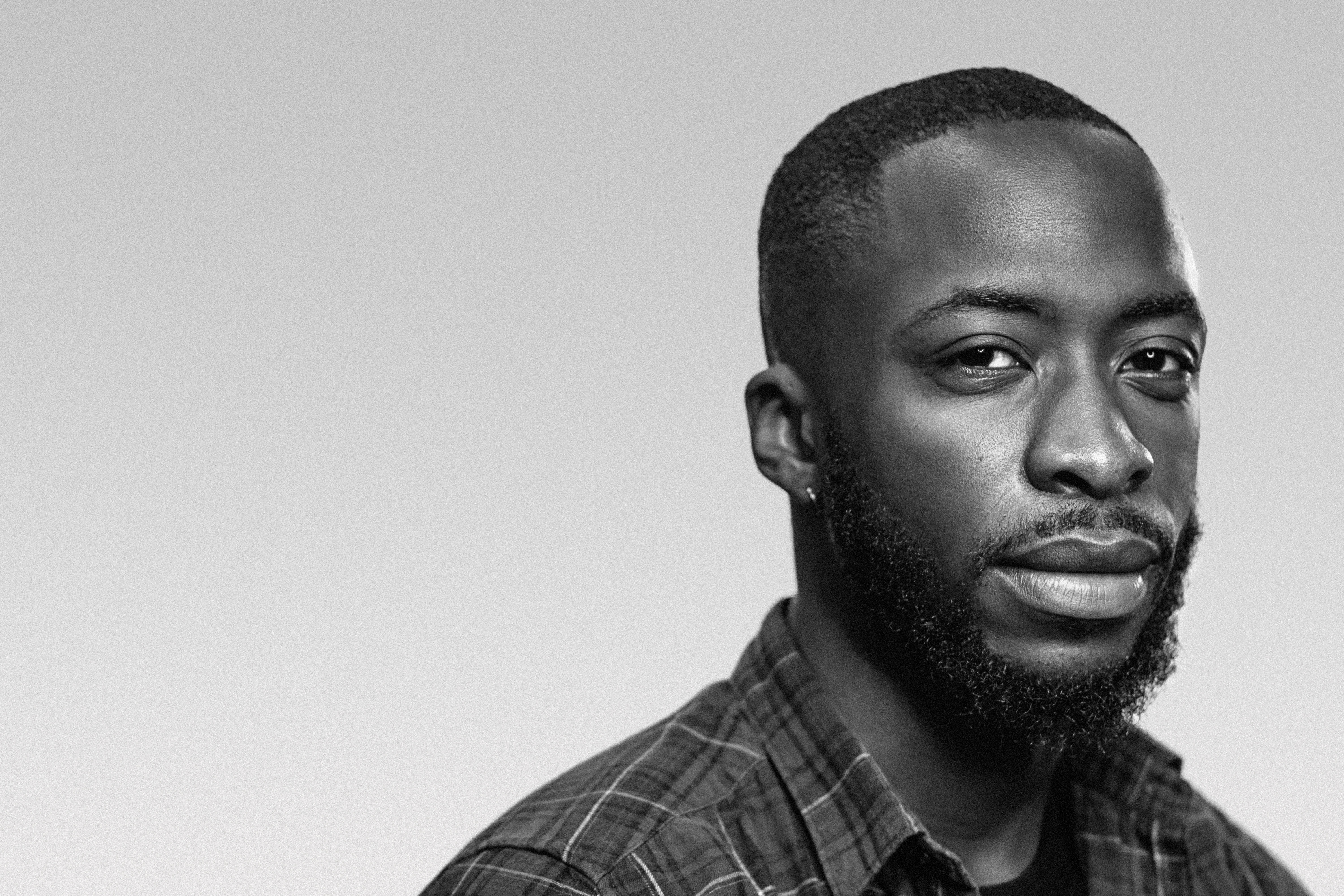 Black and white portrait of a man with short hair and a beard, wearing a plaid shirt, gazing calmly at the camera