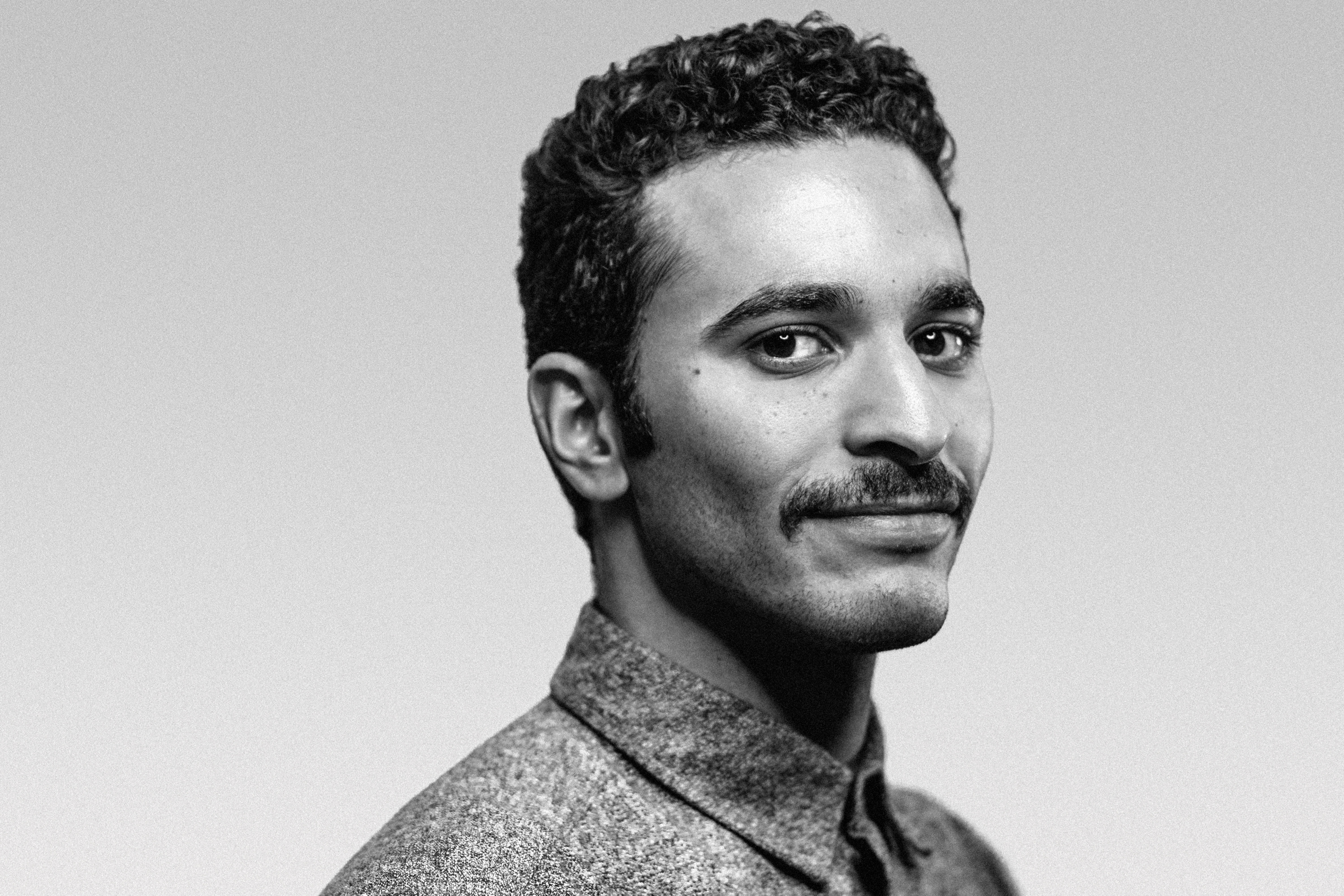 Black and white portrait of a man with short curly hair and a mustache, wearing a buttoned shirt