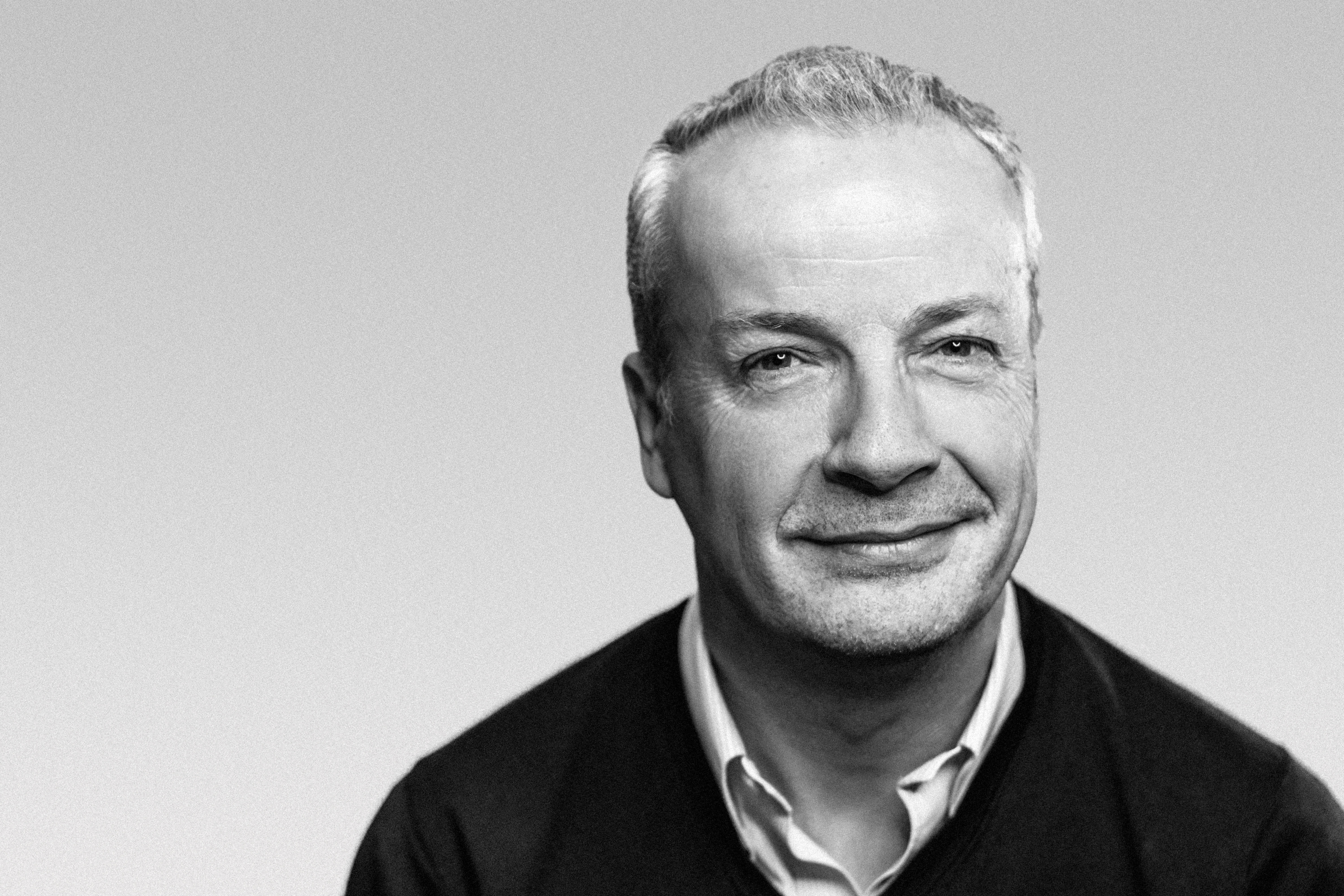 Black and white portrait of a smiling man wearing a collared shirt and sweater
