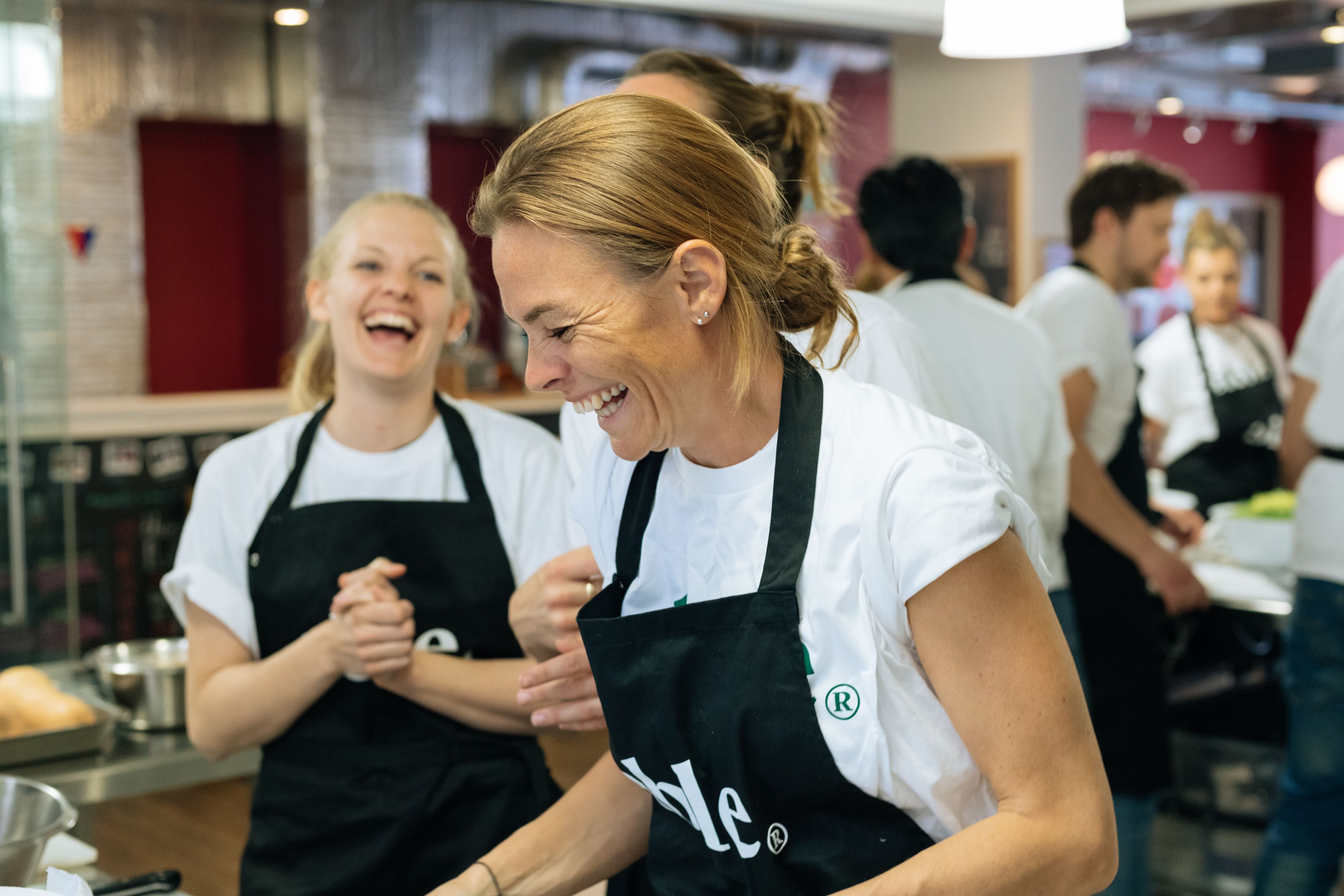 A woman wearing a black apron and white shirt is laughing.