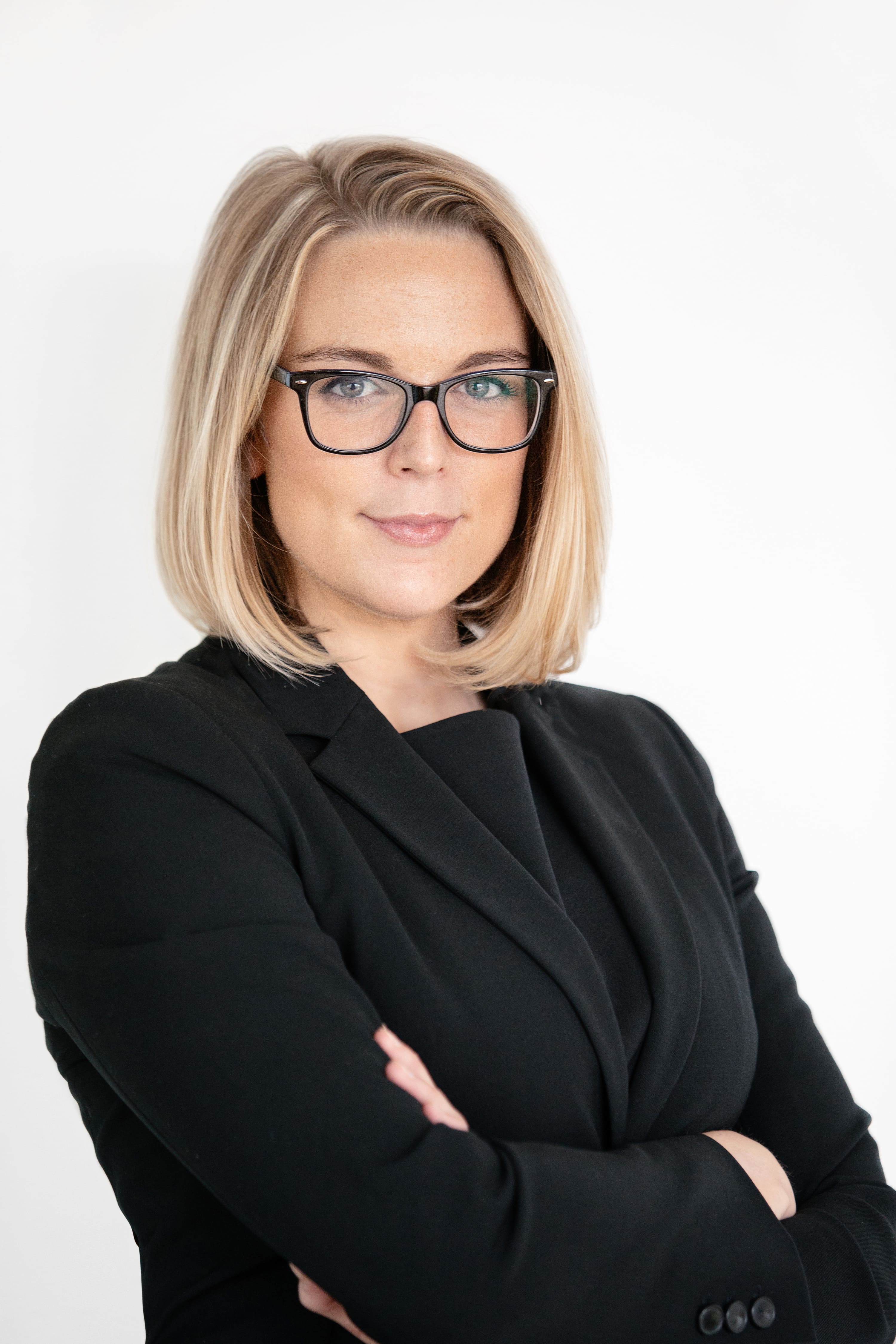 A woman wearing glasses and a black suit.