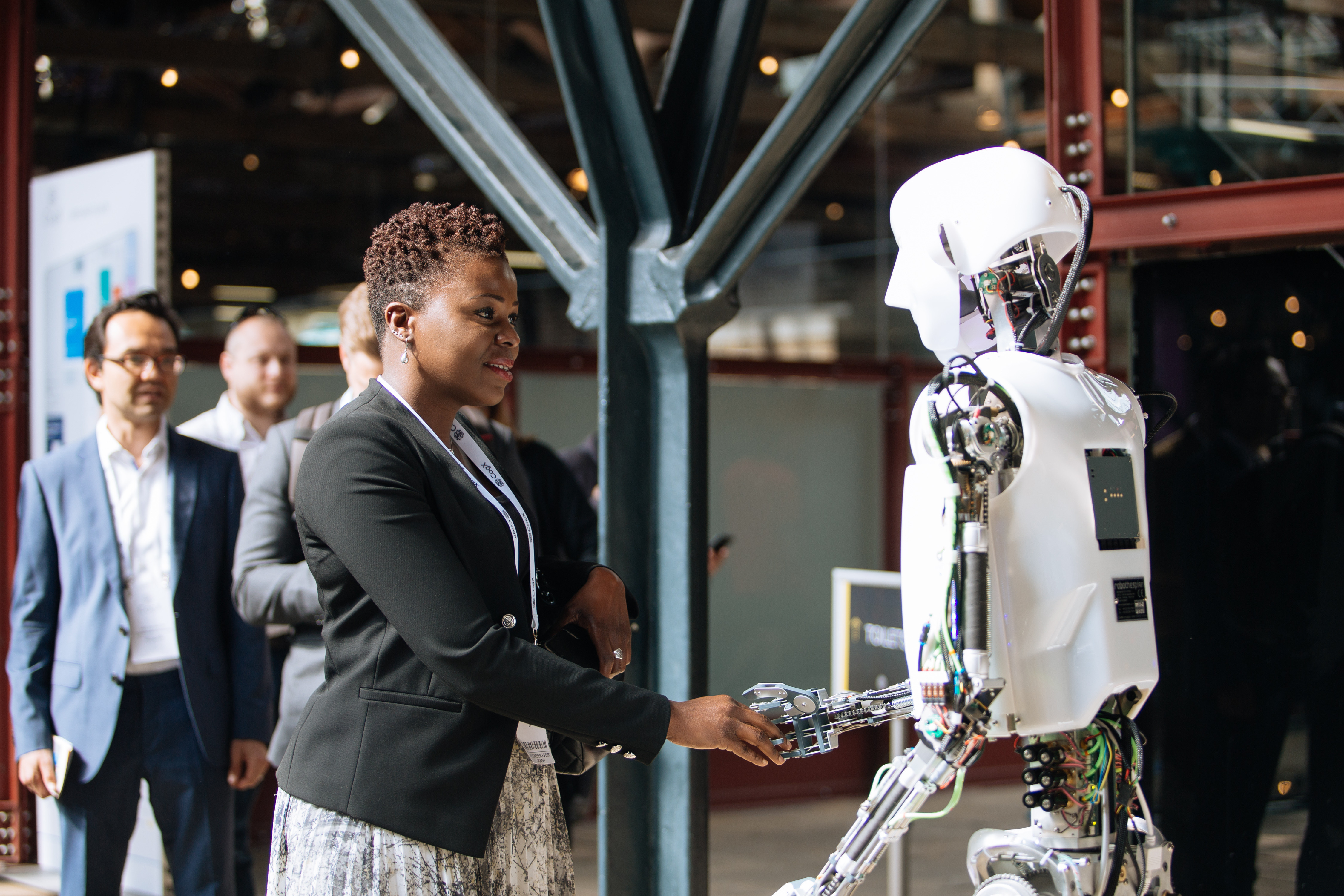 A woman in a black jacket is holding a robot's hand.