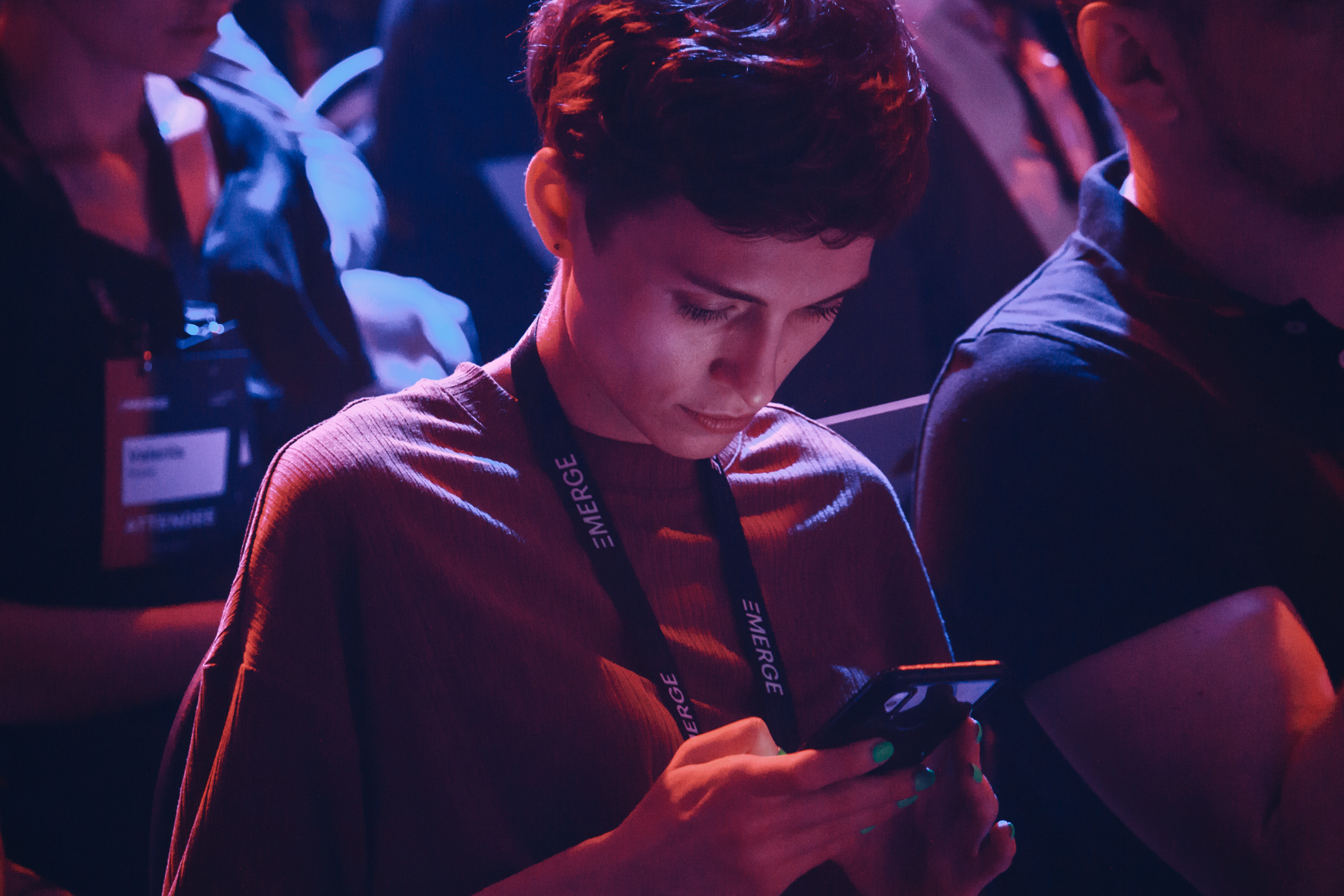 Attendee at the Emerge tech event engrossed in a mobile phone under vibrant lighting