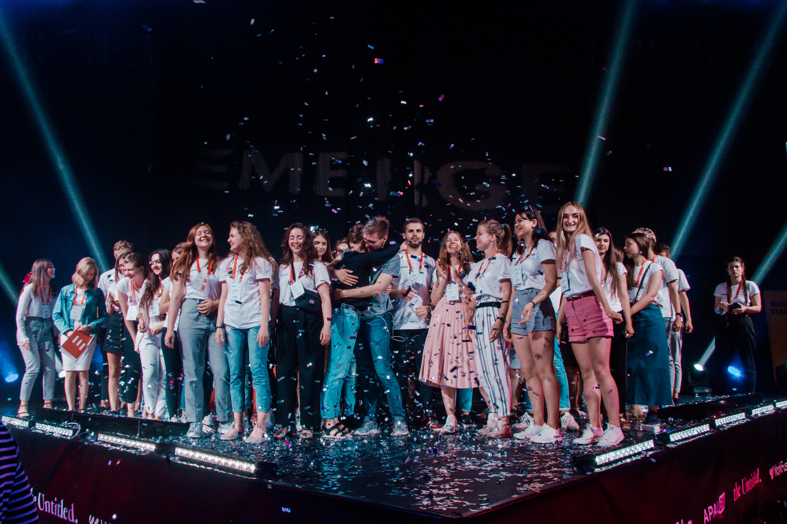 Group celebration on stage with confetti at the Emerge tech event, featuring young professionals and volunteers