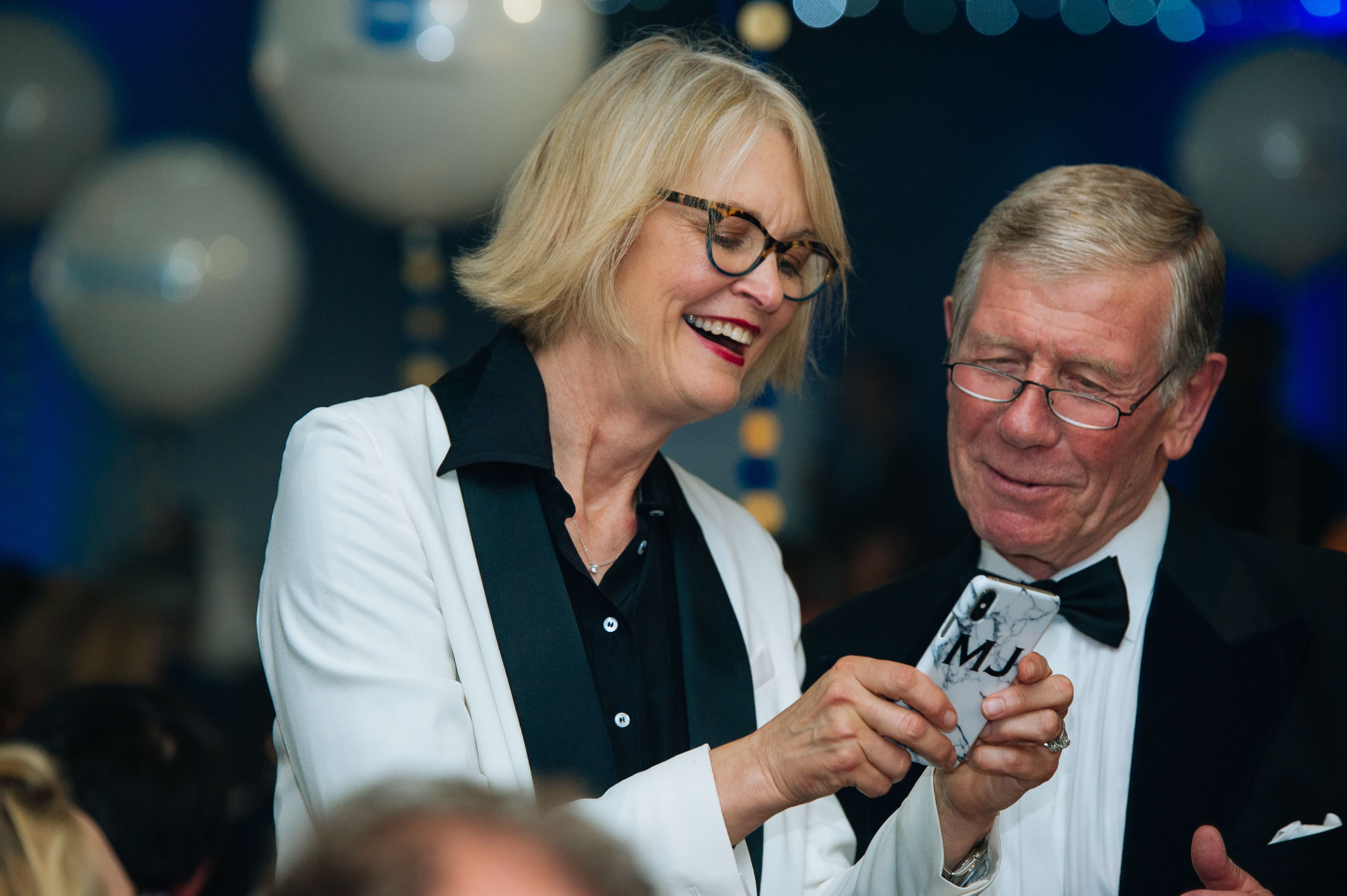 Two smiling attendees sharing a moment while viewing a phone at a formal networking event