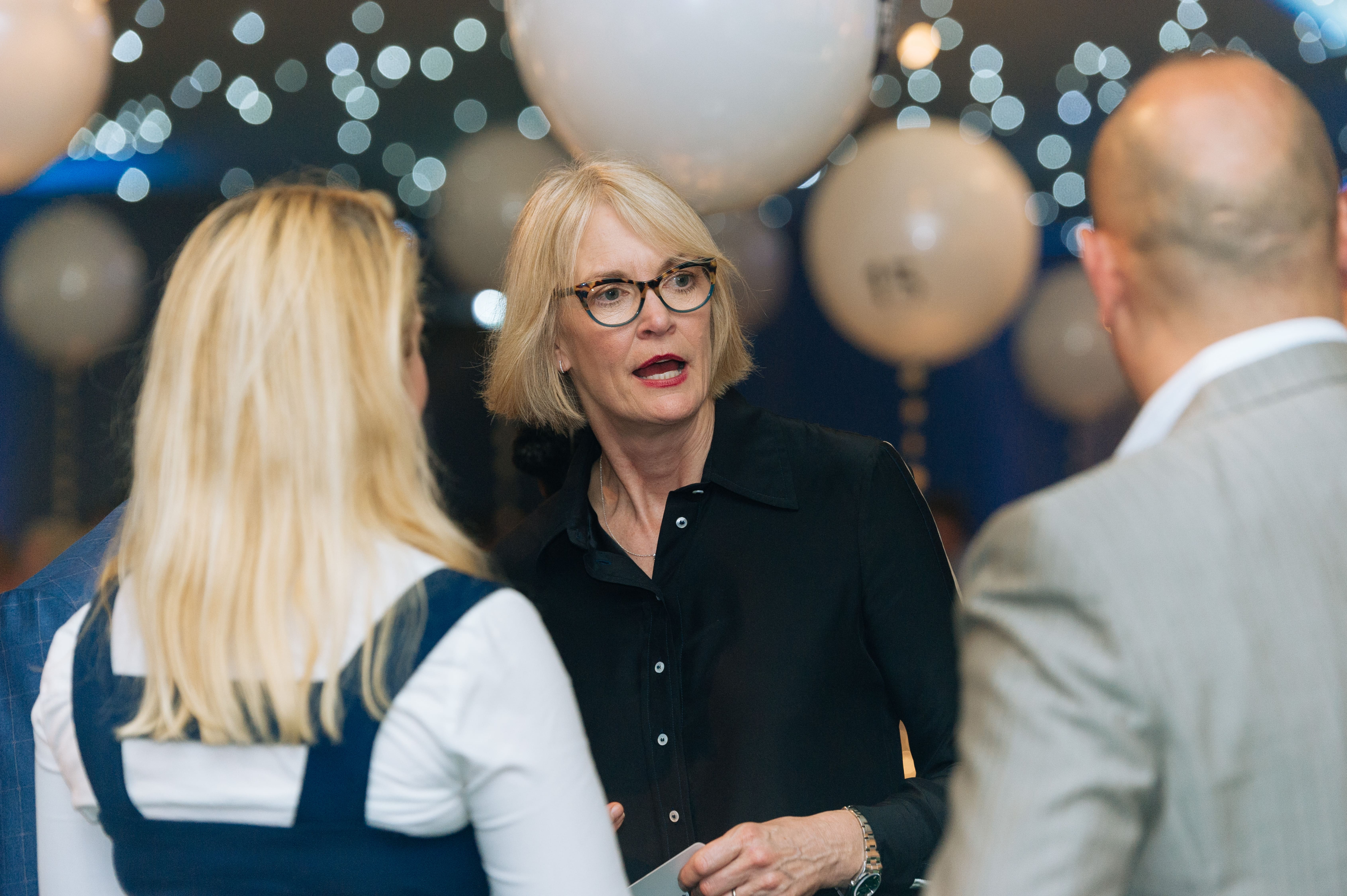 Professional woman engaging in conversation at a networking event with decorative lighting and balloons