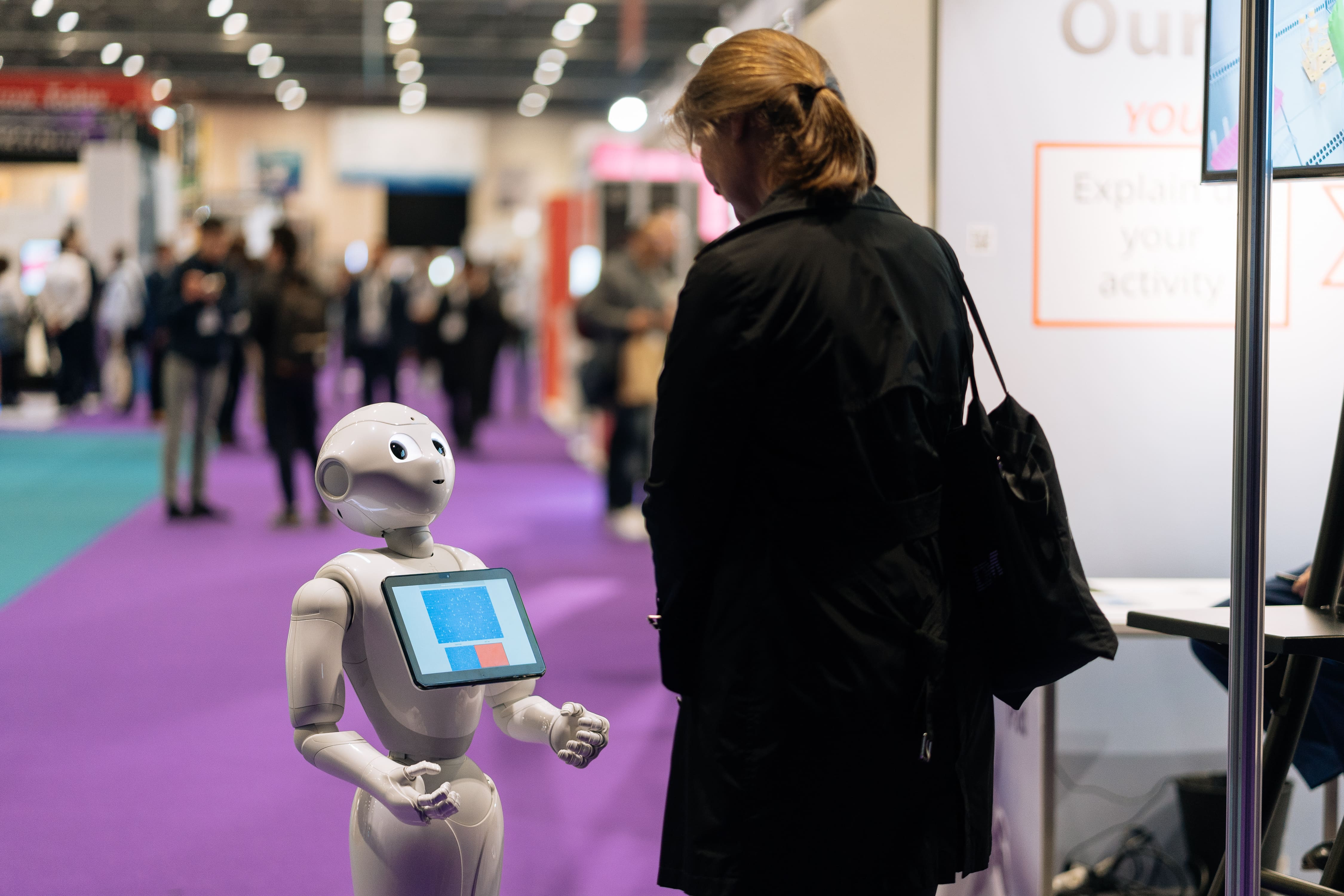 Interactive humanoid robot engaging with a visitor at a tech exhibition on a vibrant purple carpet
