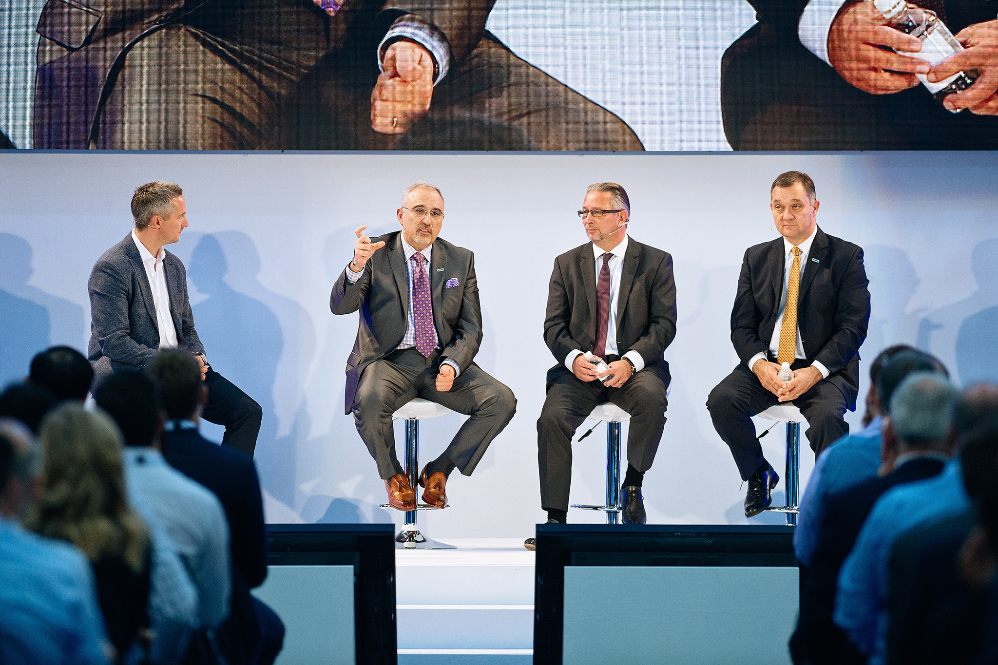 A group of men in suits are sitting on stools.