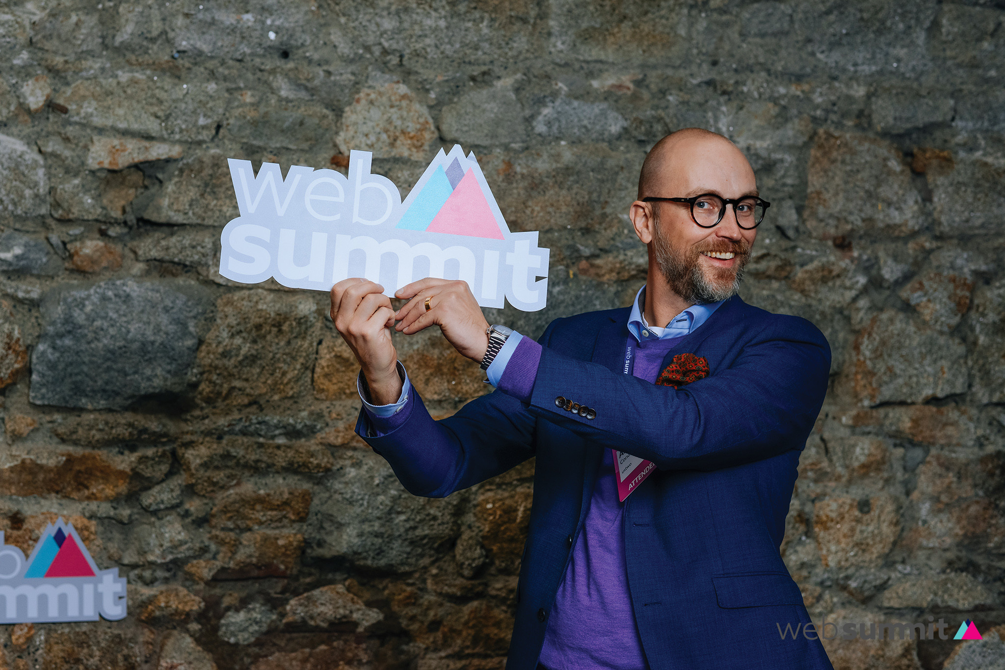 A man wearing a purple shirt and a suit holding a sign that says web summit.