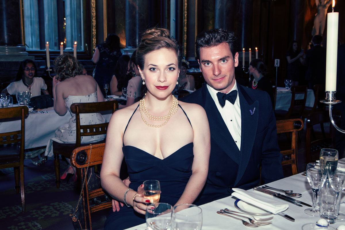 A man and woman sit at a table with wine glasses and forks.