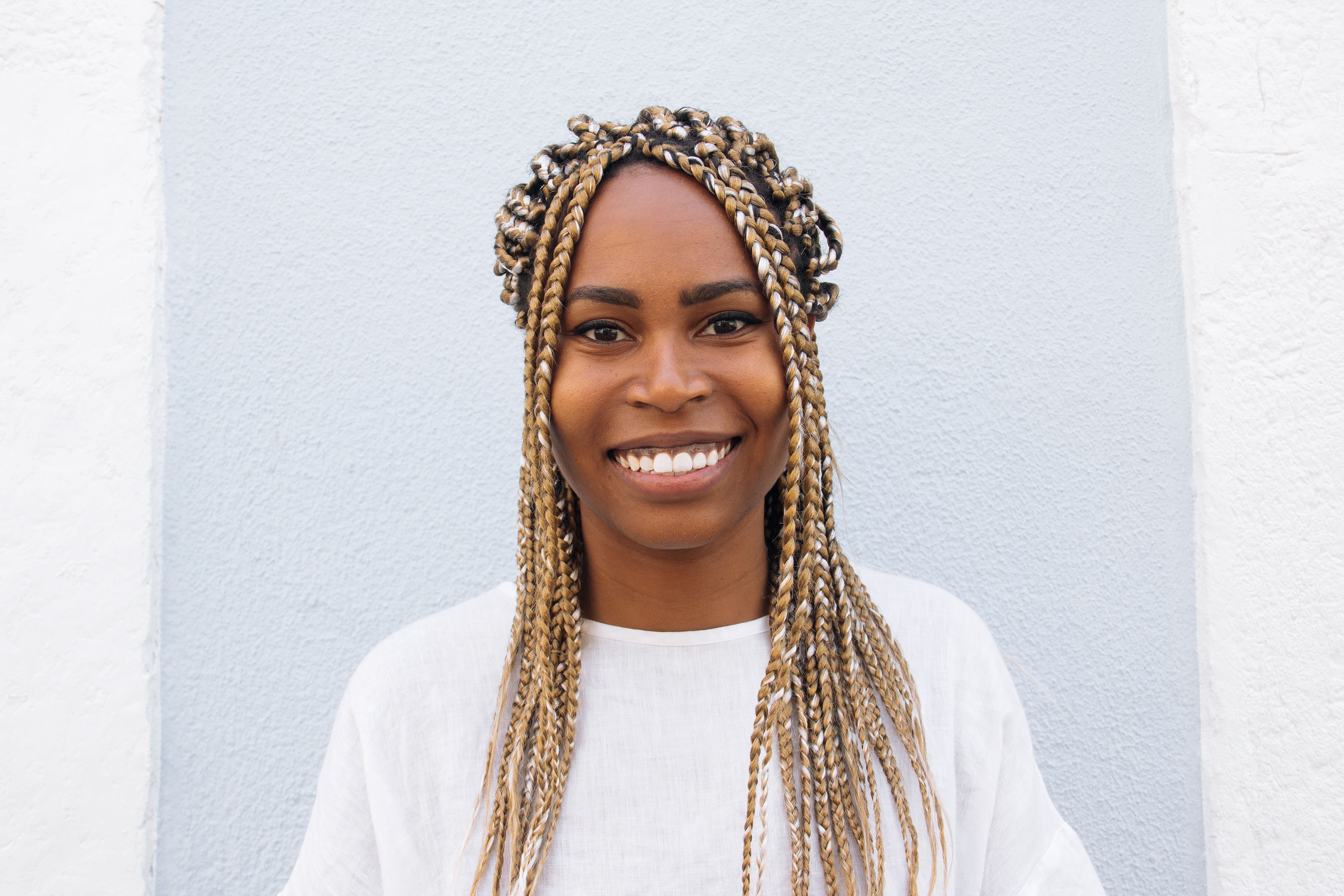 Portrait of a smiling woman with long blonde braids, standing against a light-colored background