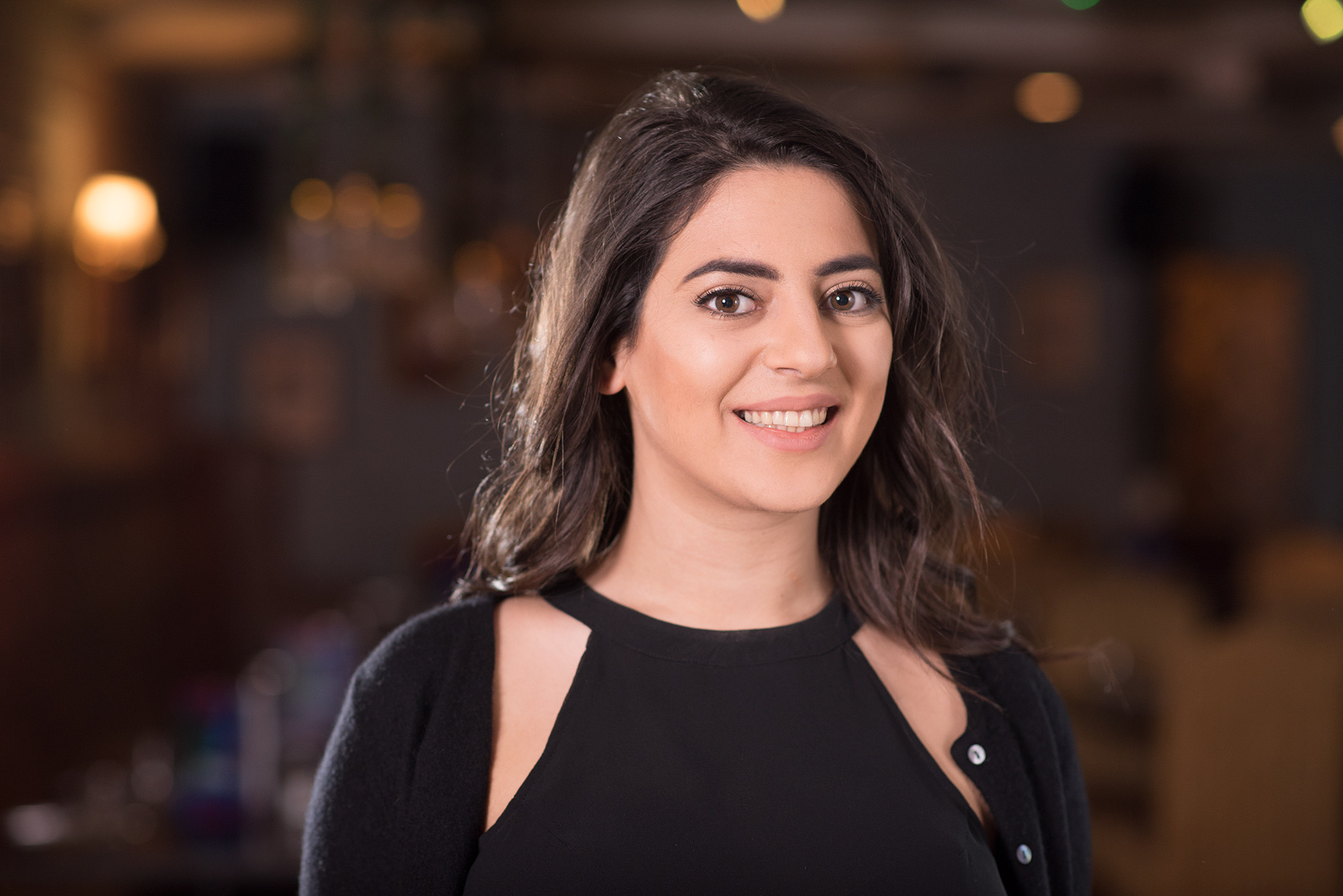 Smiling woman with long dark hair posing indoors with a softly lit background