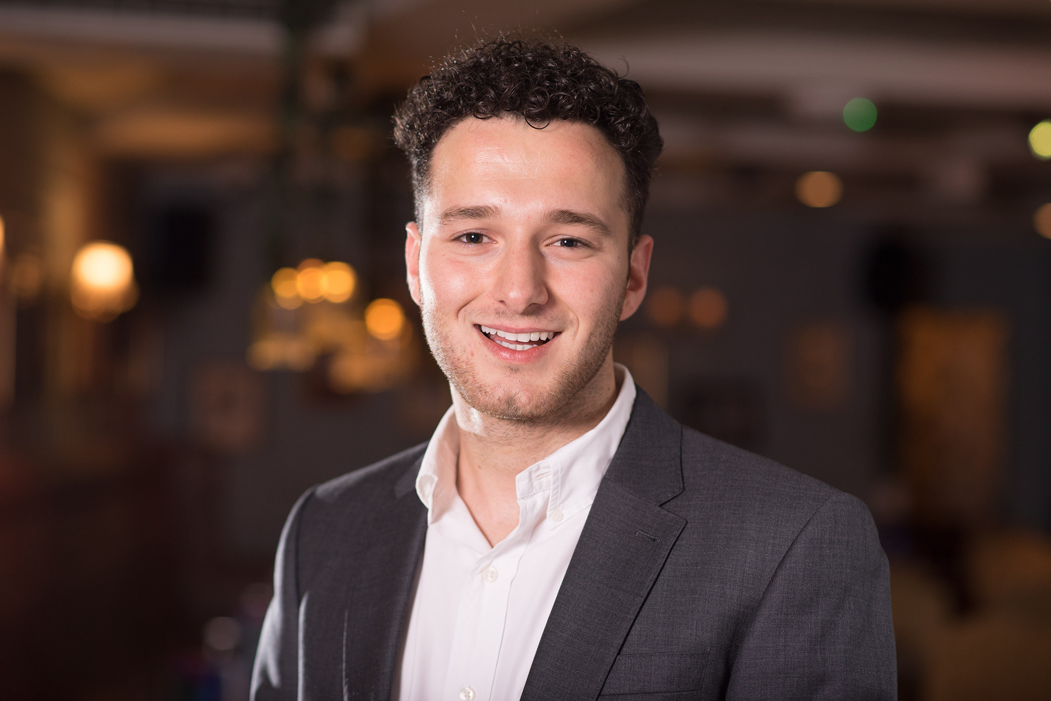 Smiling man in a suit posing indoors with warm ambient lighting in the background