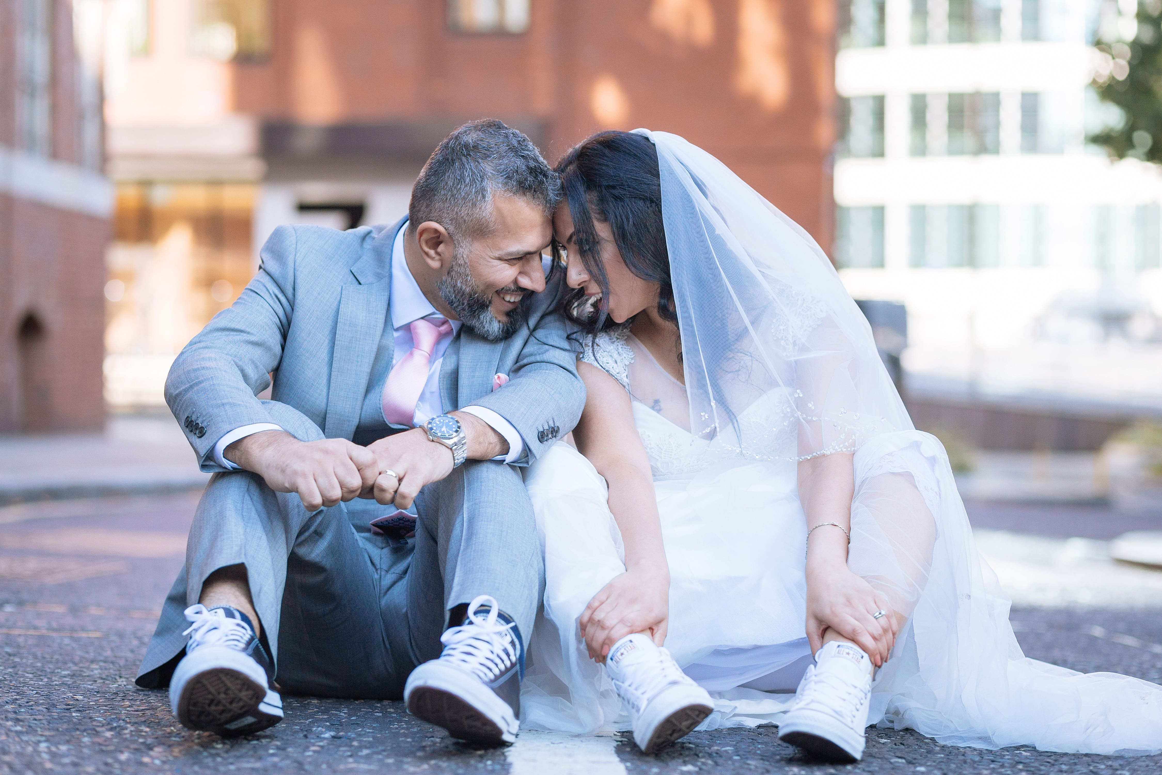 A man and woman wearing wedding dresses and tuxedos sit on the ground.
