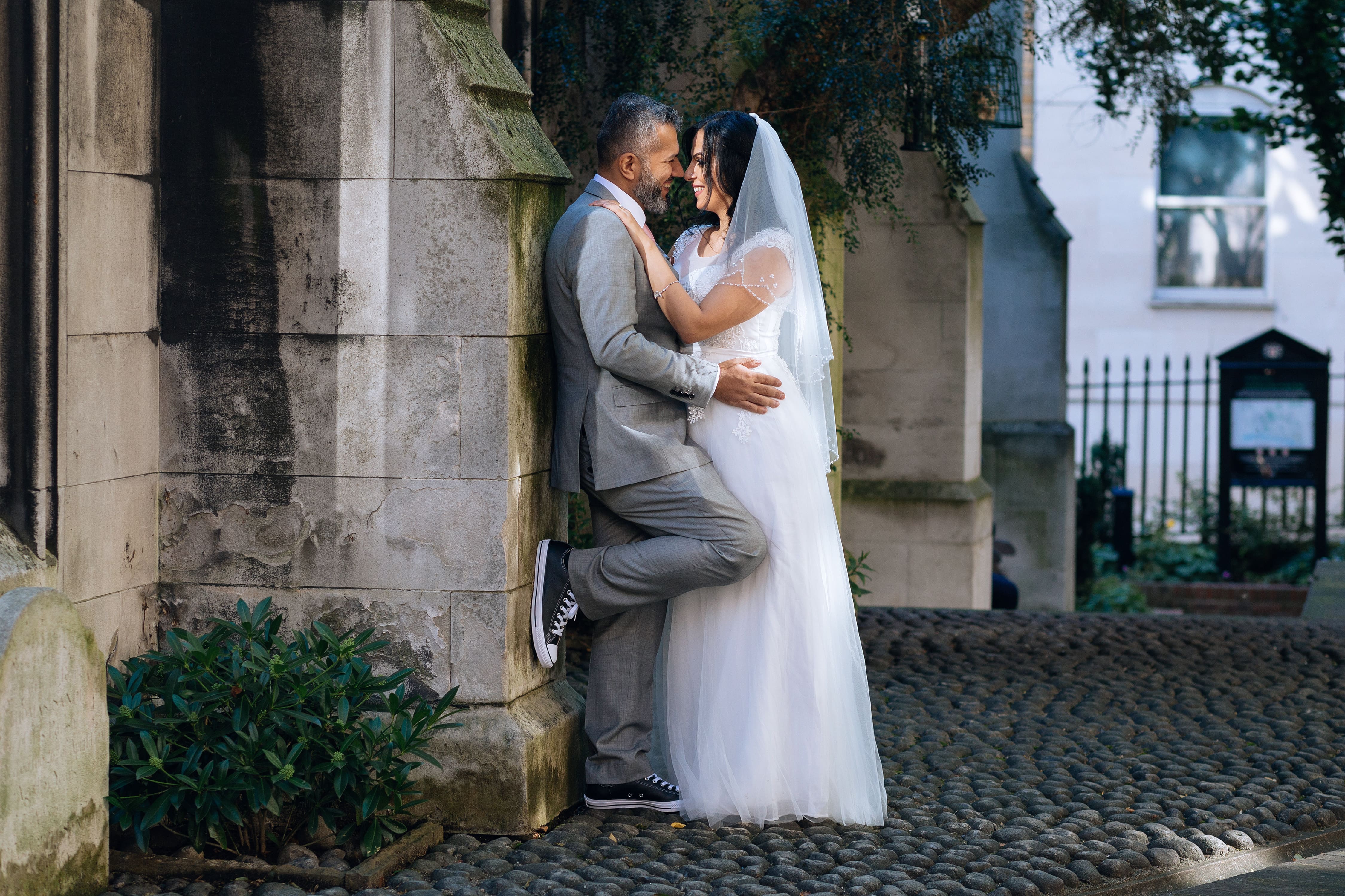 A bride and groom lean against a stone pillar.