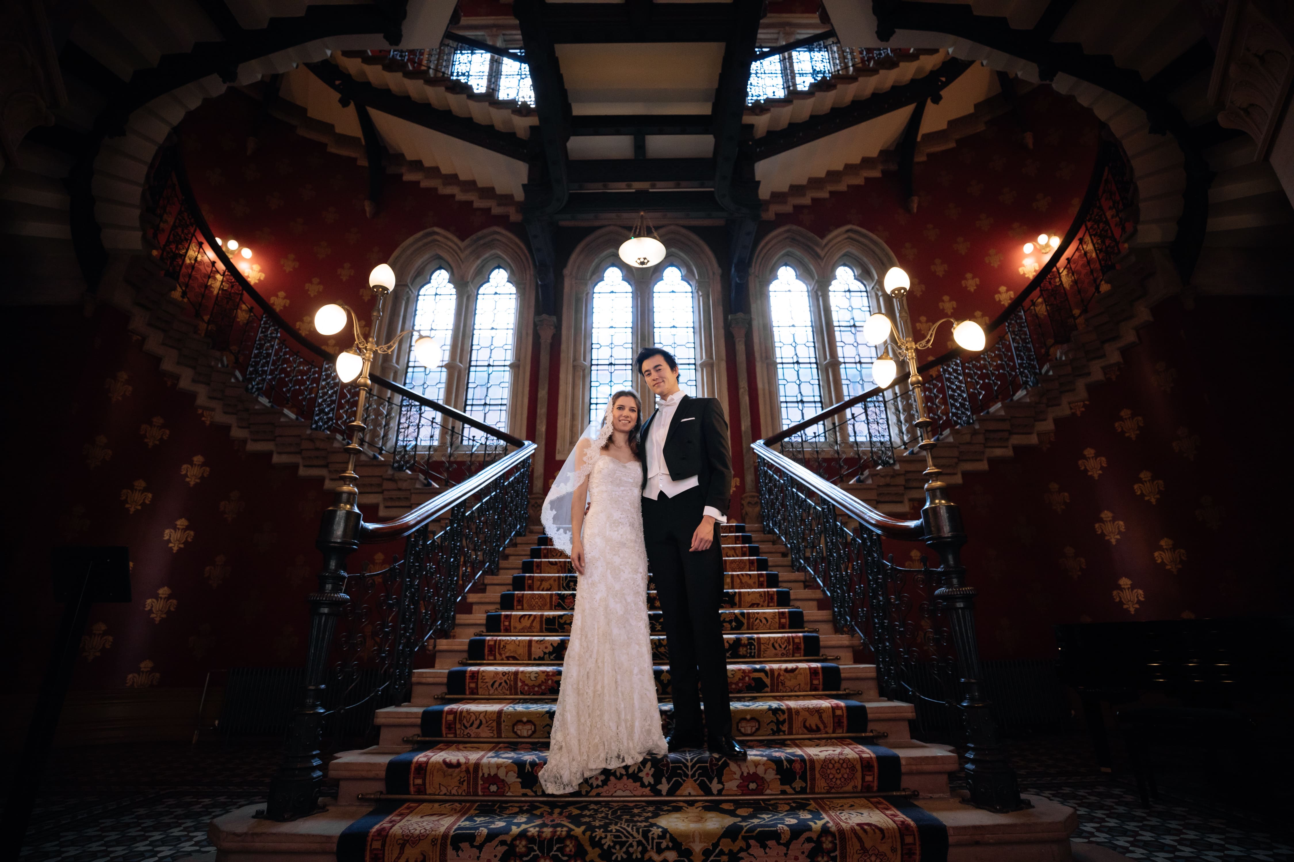 A bride and groom stand on a staircase in front of a castle.