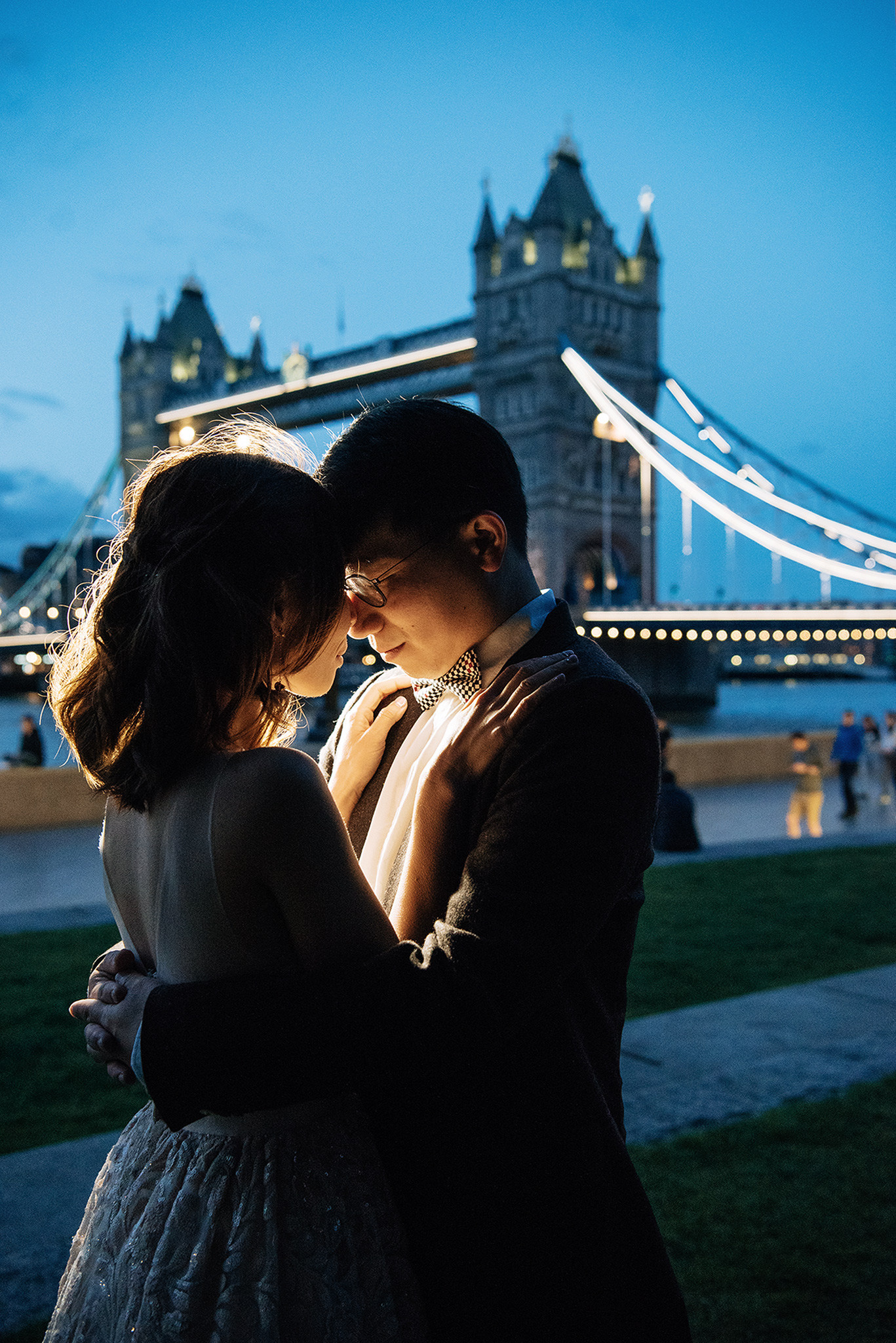 A couple standing in front of a bridge with the man wearing a bow tie.